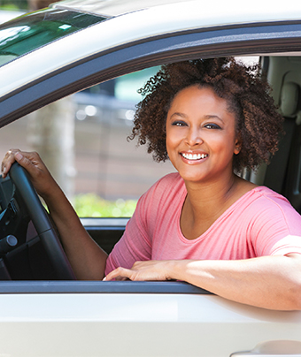 Smiling woman inside a car holding the steering wheel