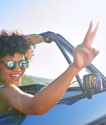 Smiling woman inside a drop top convertible holding up a peace sign