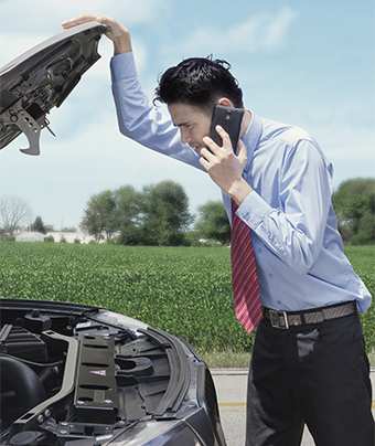 Man on the phone while holding open the bonnet cover of a car with vegetation in the background